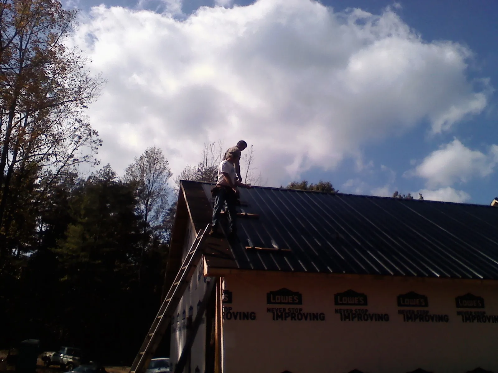 Roofer fastening dark metal panels high against a cloudy sky, from a Roof Inspection job in Auburn